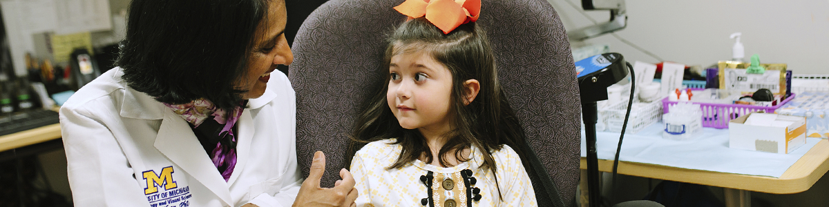 Naheed Kahn talking to a little girl who is sitting in an examination chair